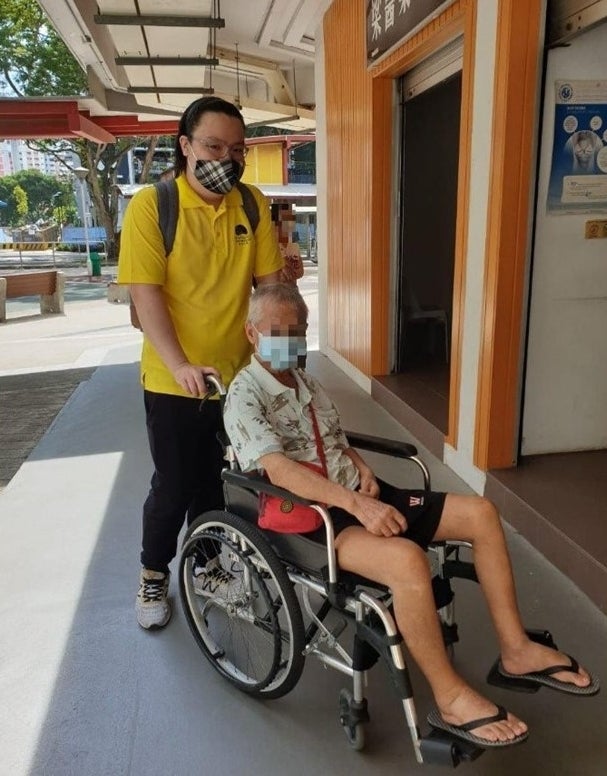 alt="Jordon Ong volunteering with Seniors Befriending and pushing a man in a wheelchair"